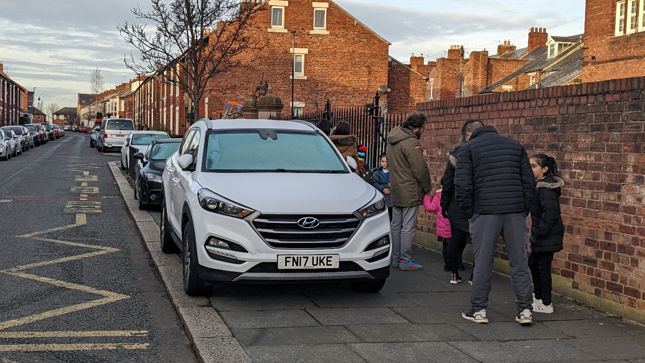 Cars parking on the pavement at the entrance to Chillingham Road Primary School. There is little room for parents, grandparents and carers to wait for their children. The pavement is also used by children walking to school.